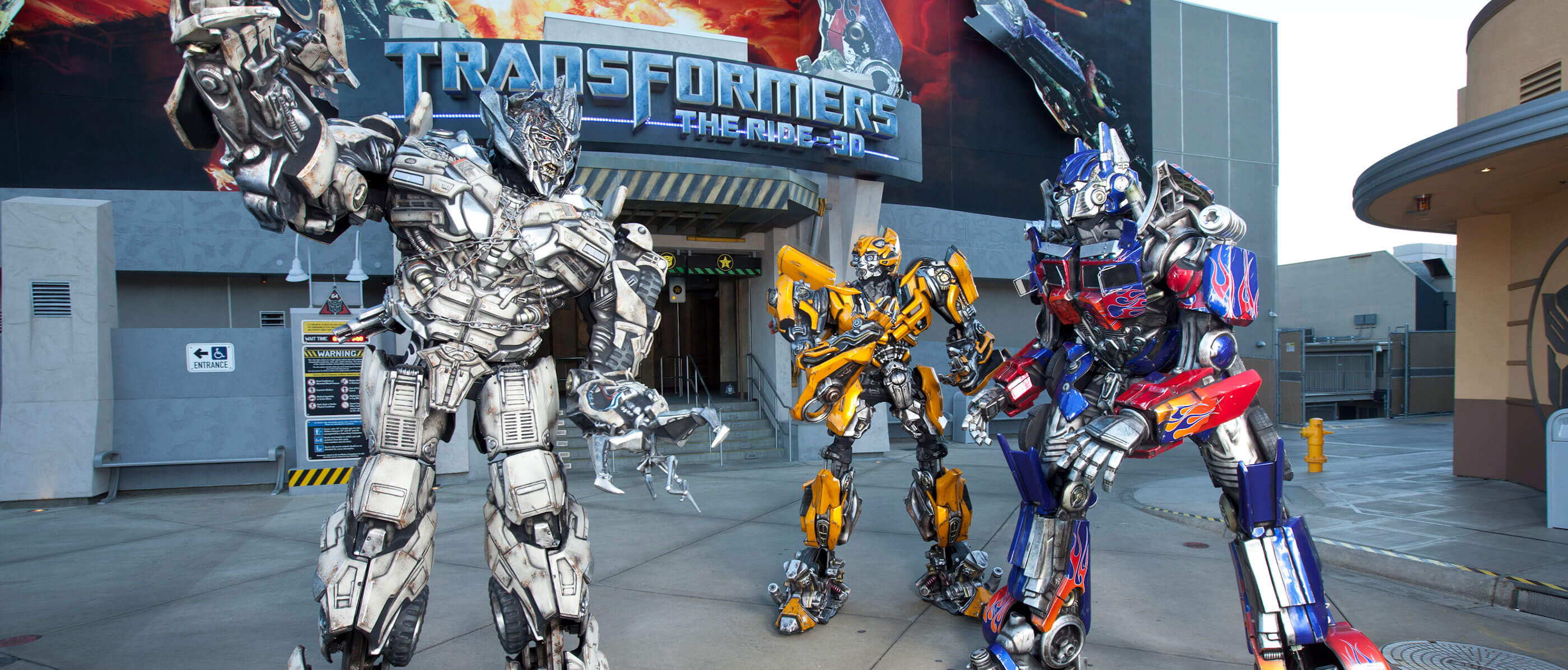 Three Transformer characters in front of the Transformers The Ride 3D entrance.