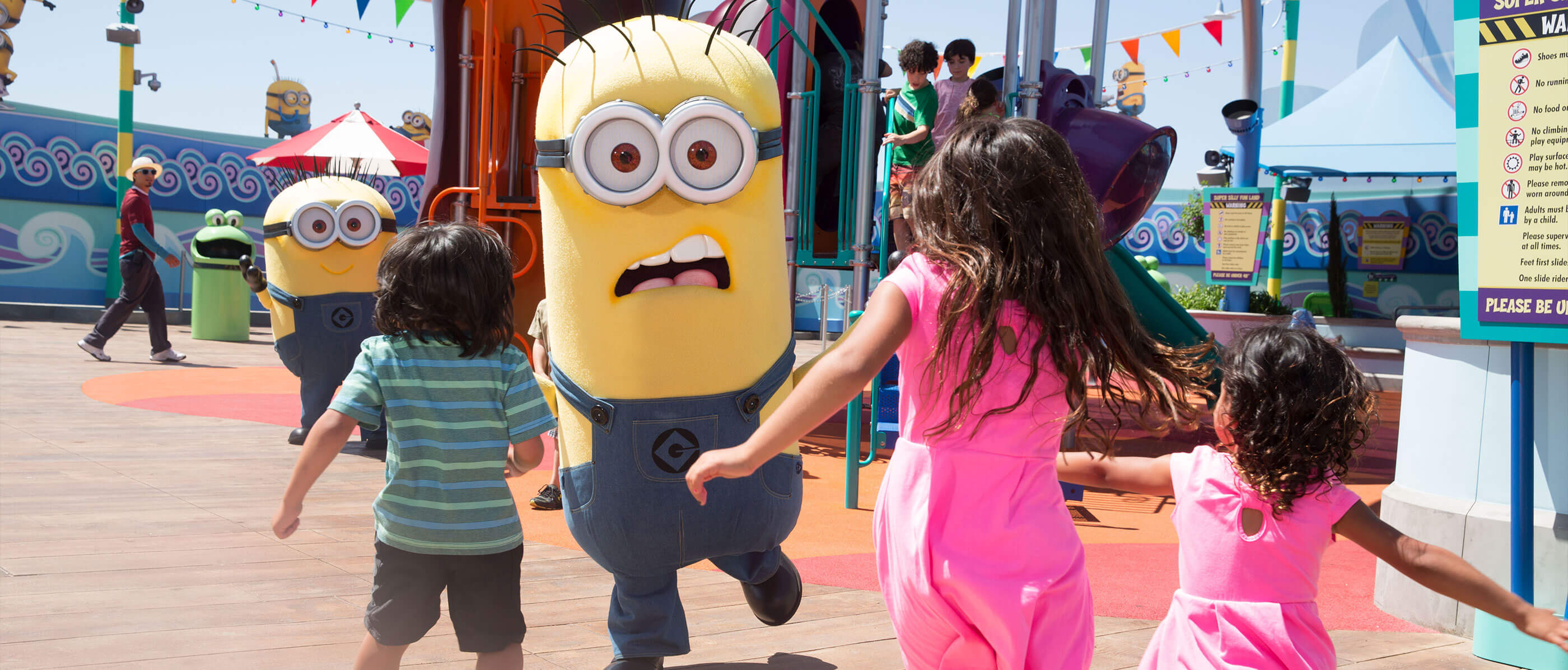 Three kids running towards two minions on a sunny day.