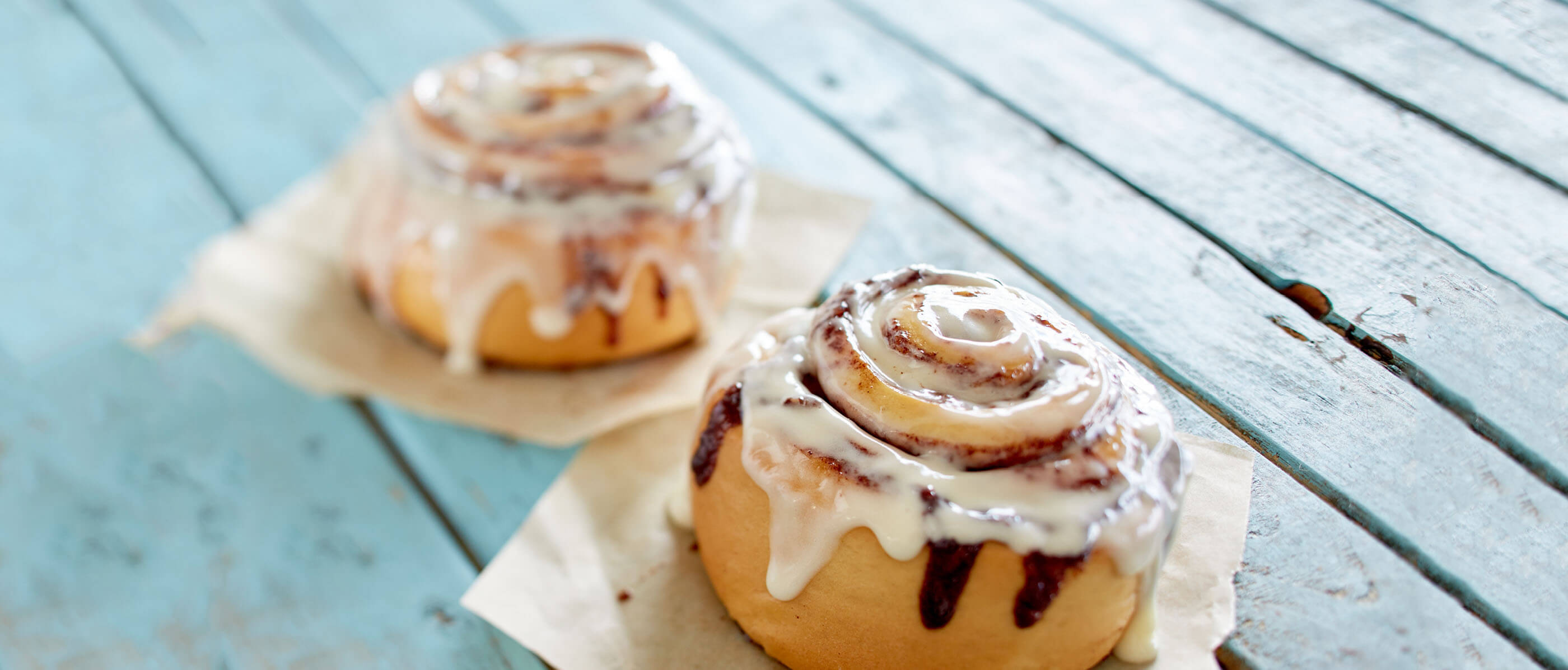 Two cinnamon buns on a blue wooden deck.