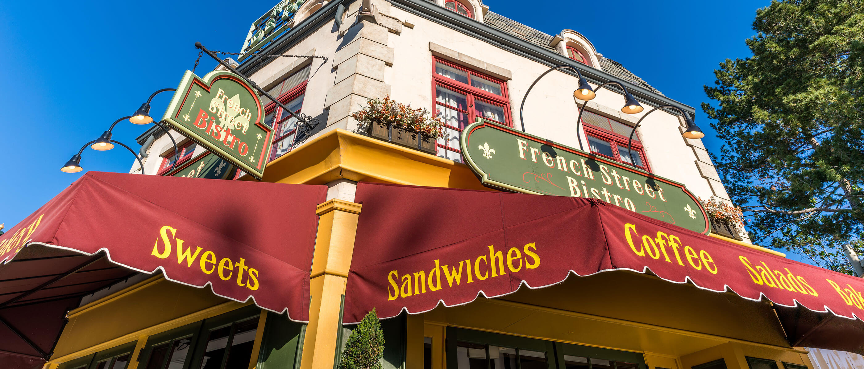 A building with the sign French Street Bistro and a canopy with sandwiches, coffee, salads and baked goods on it in yellow writing.