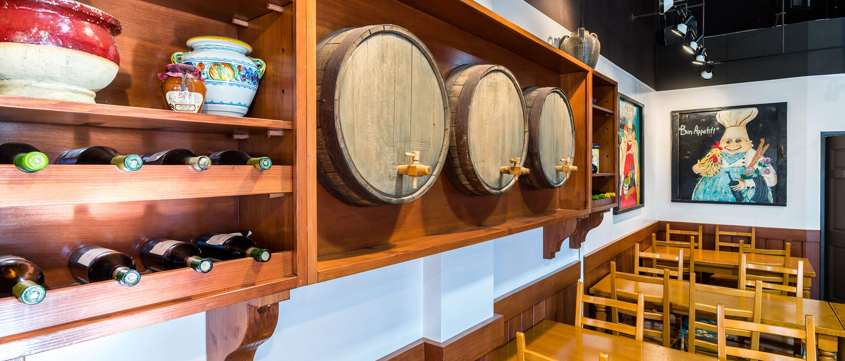 Three beer wooden kegs in the wall, beside a wine rack with tables and chairs underneath.