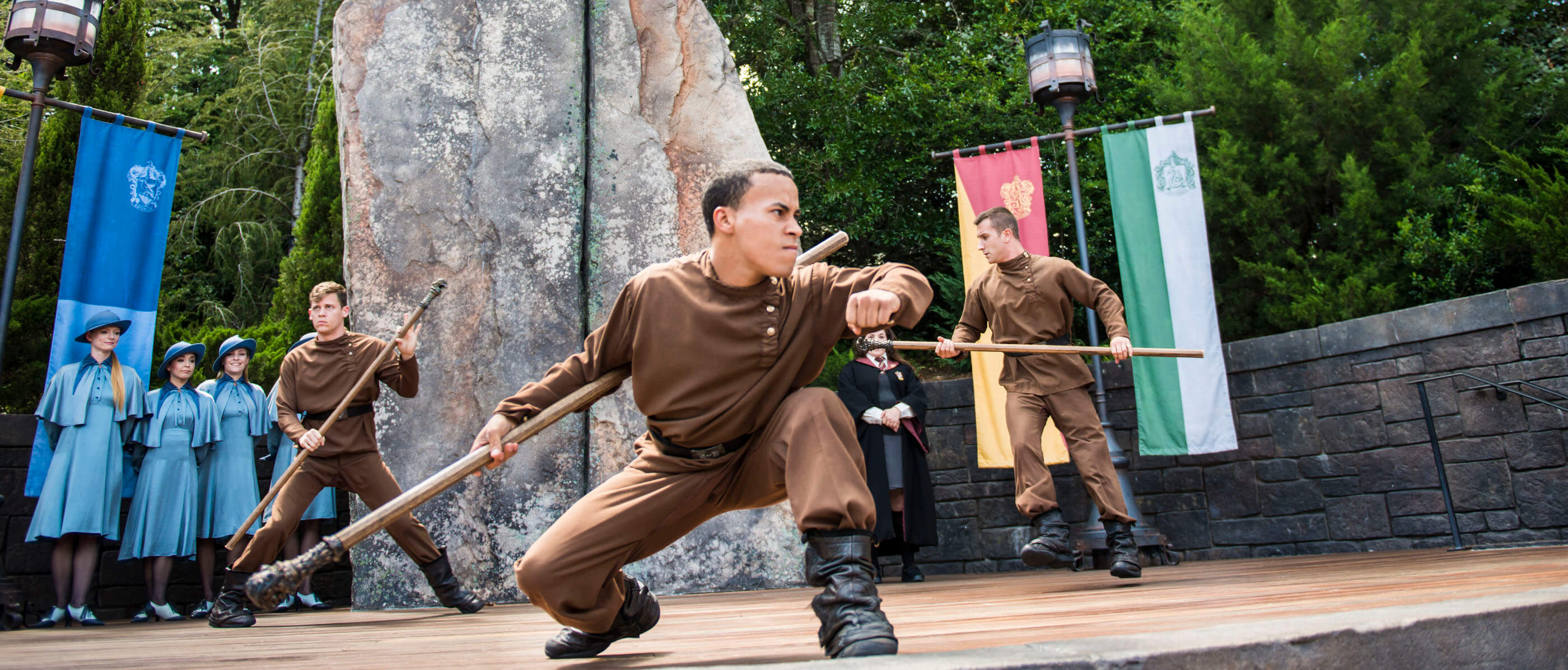 Three people dressed up as the Durmstrang Harry Potter characters, one low to the ground with a pole in his hand.