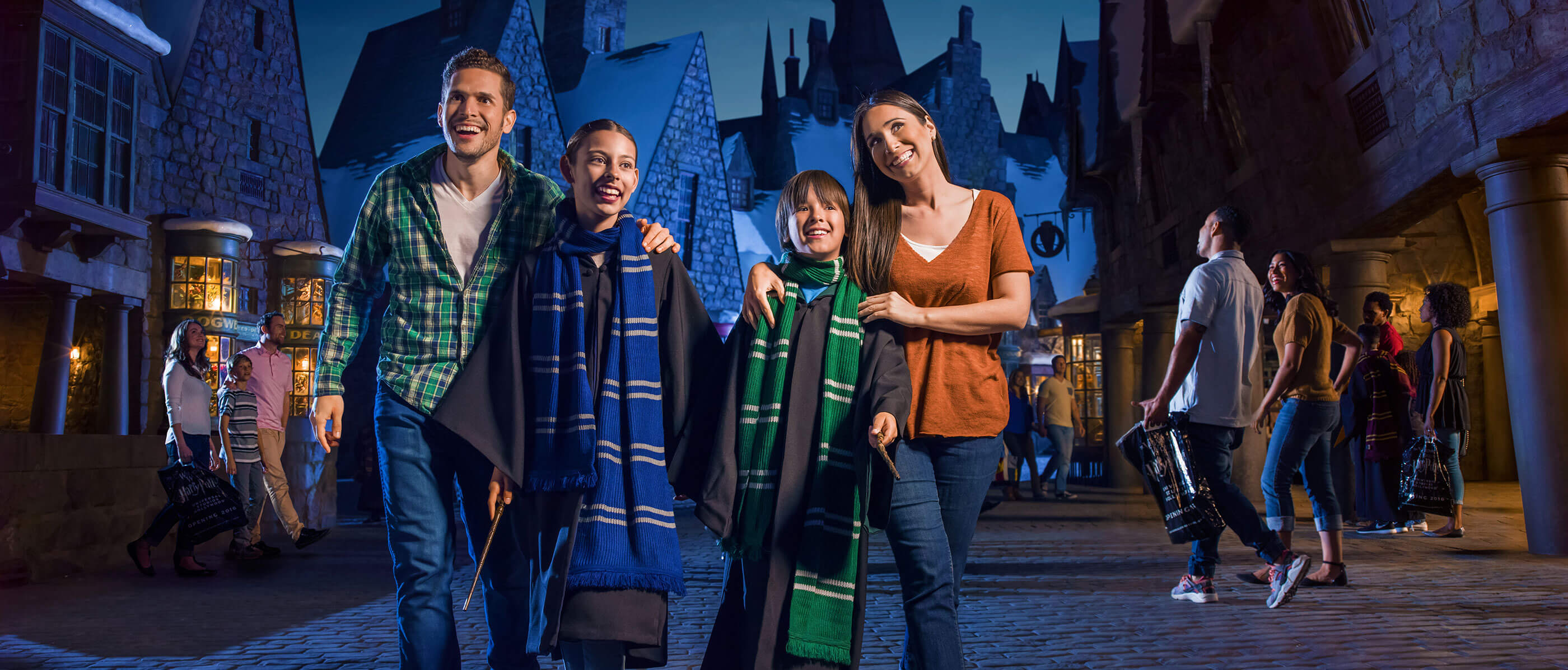 Family with two young boys dressed up as Harry Potter characters and a dark blue buildings behind them.