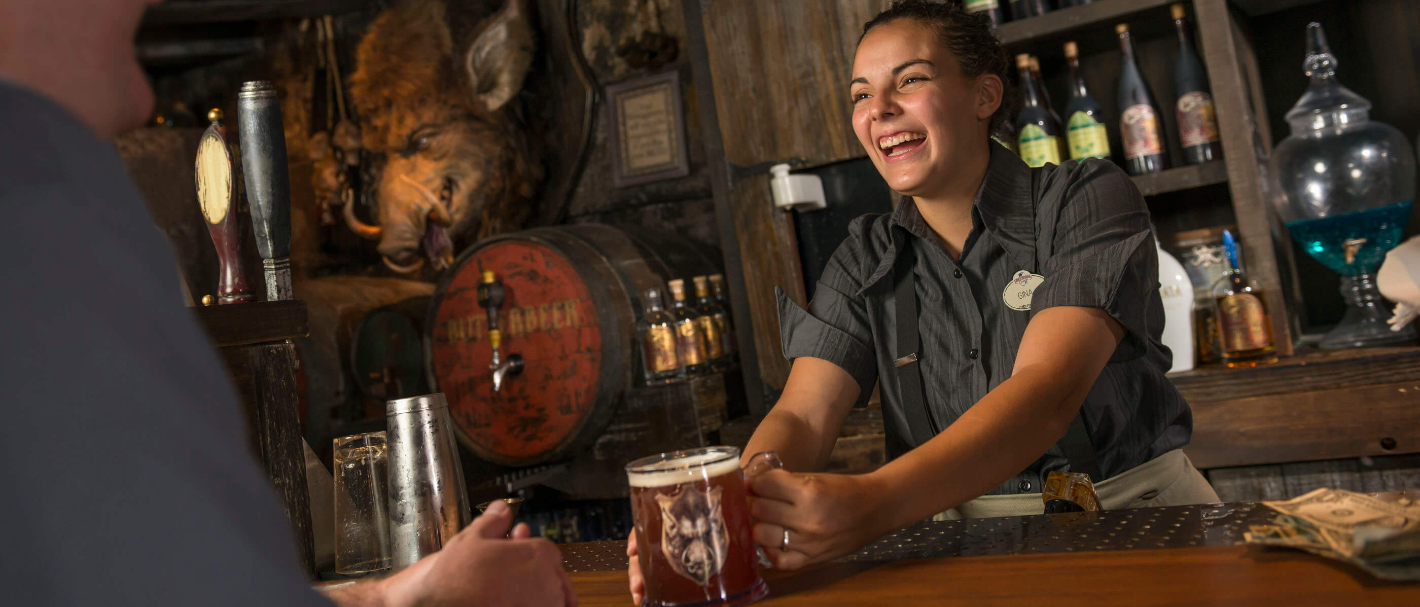 A woman smiling and handing a beer to a customer with a bar behind her.