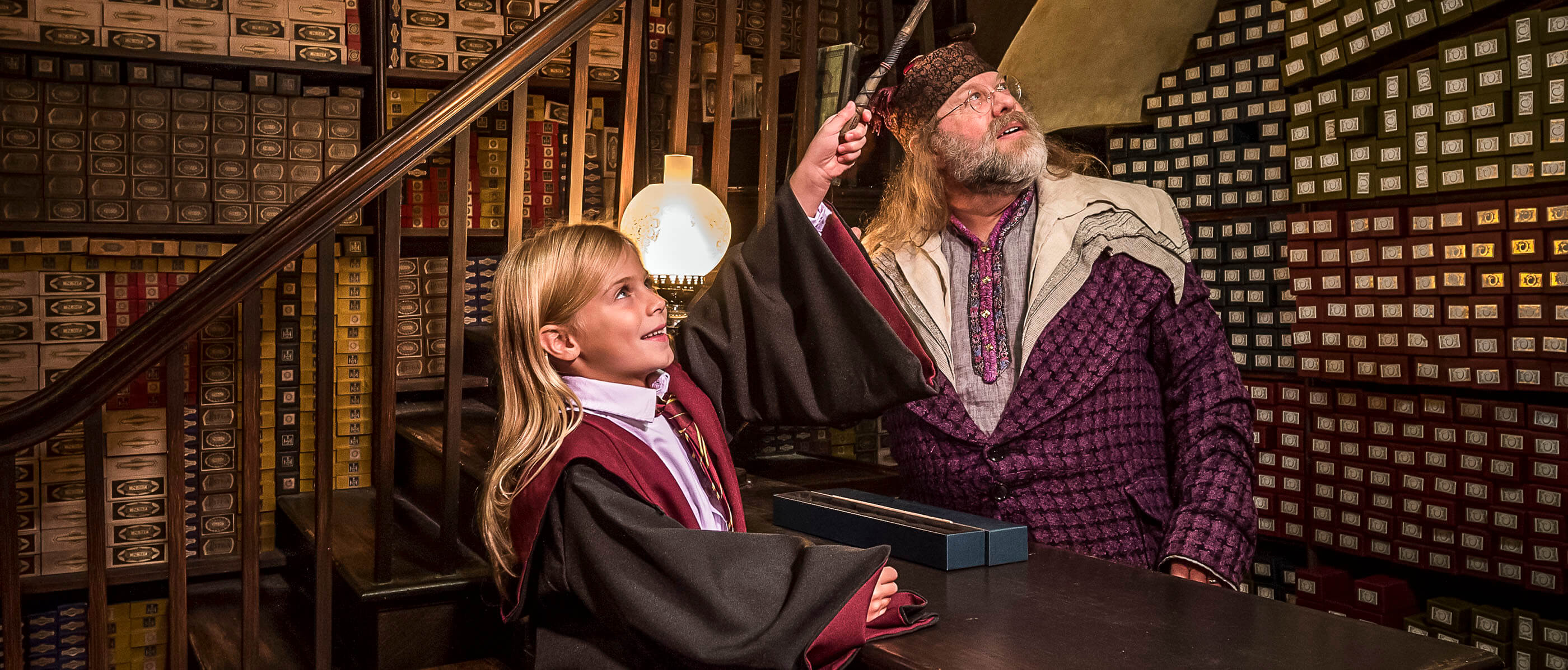 A girl holding a wand and a man looking up in the Ollivanders Wand store.