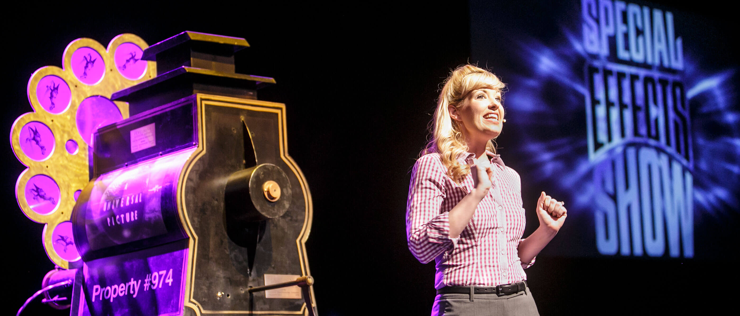 A woman on stage with the Special Effects Show logo in the background and a black object beside her.