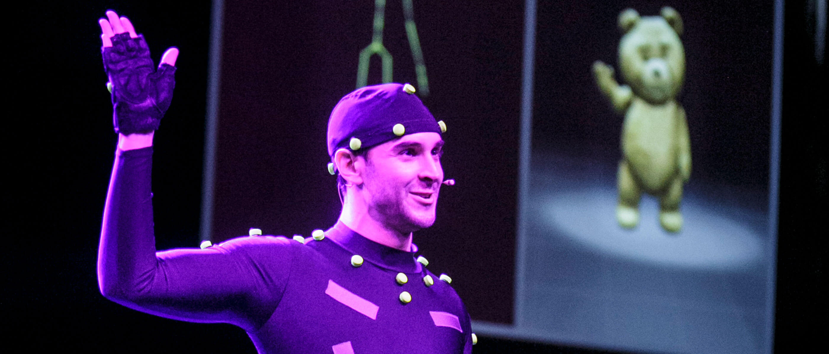 A man in a black tight suit with green dots and a digital bear in the background.