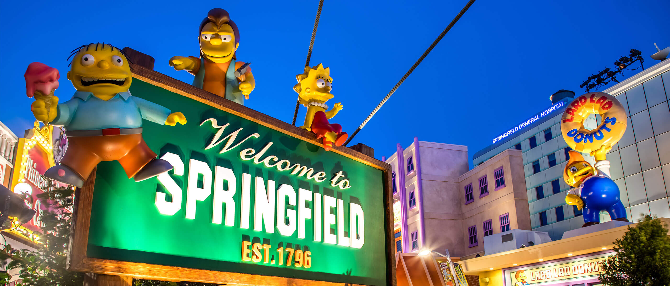The Welcome to Springfield sign and Lard Lad Donuts are brightly lit under a night sky.