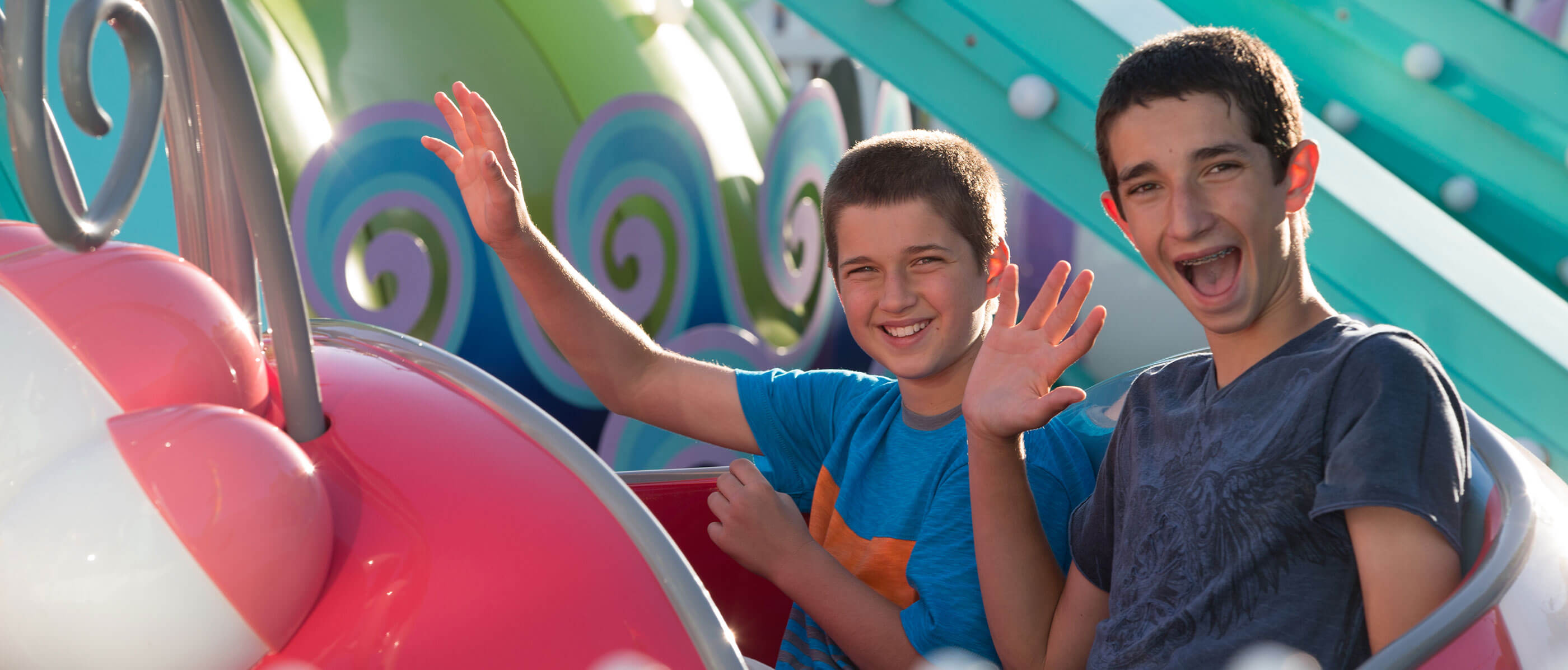 Two boys on a theme park ride in a pink cart.