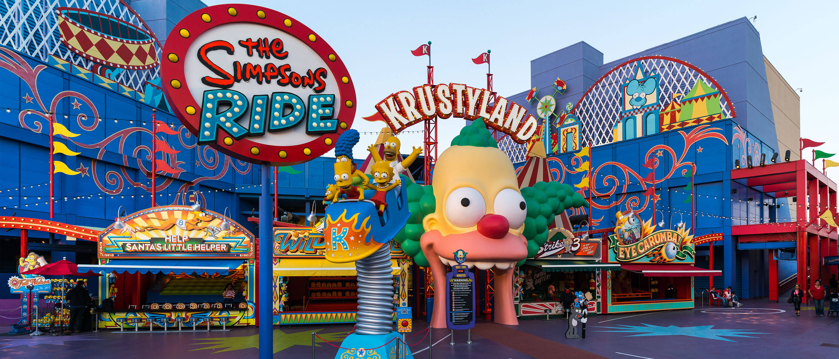 The front of the Simpsons Ride with a giant clown head over the arch way.