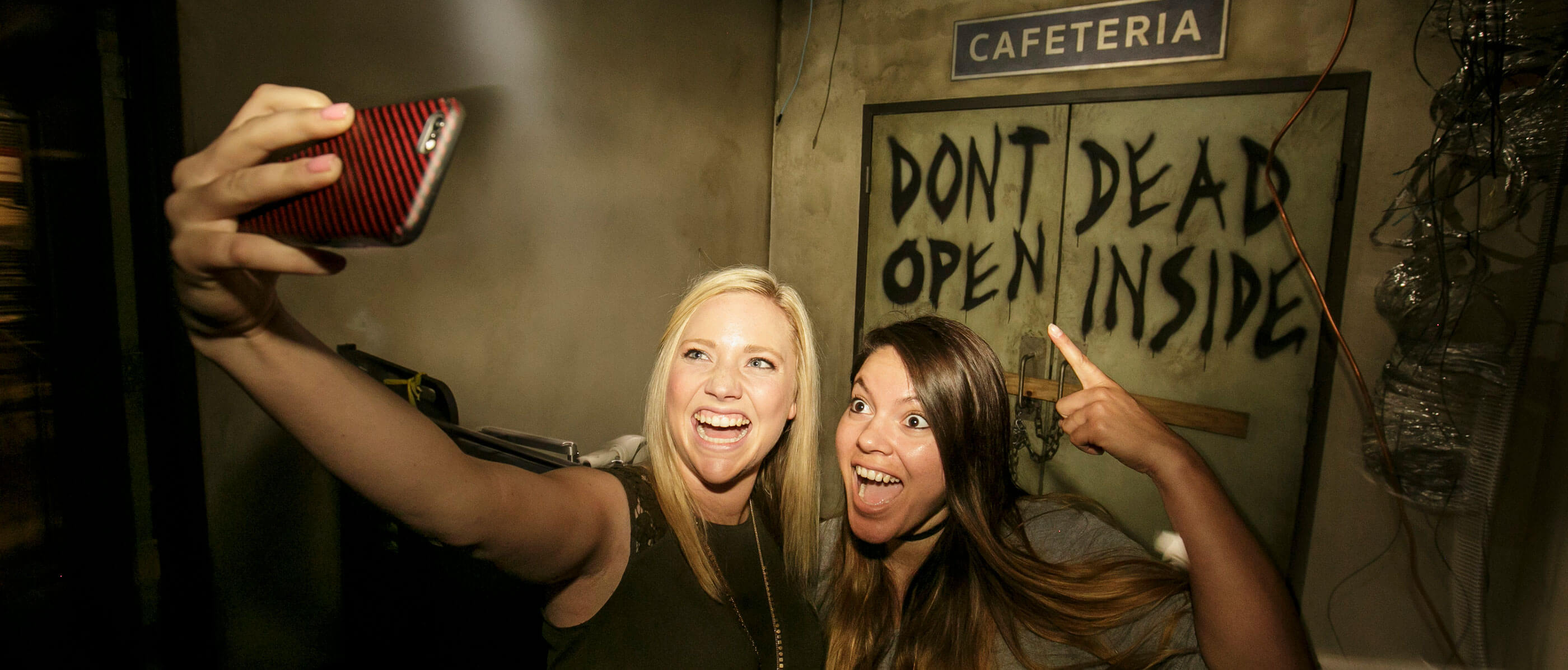 Two girls taking a selfie in front of two doors with writing saying
