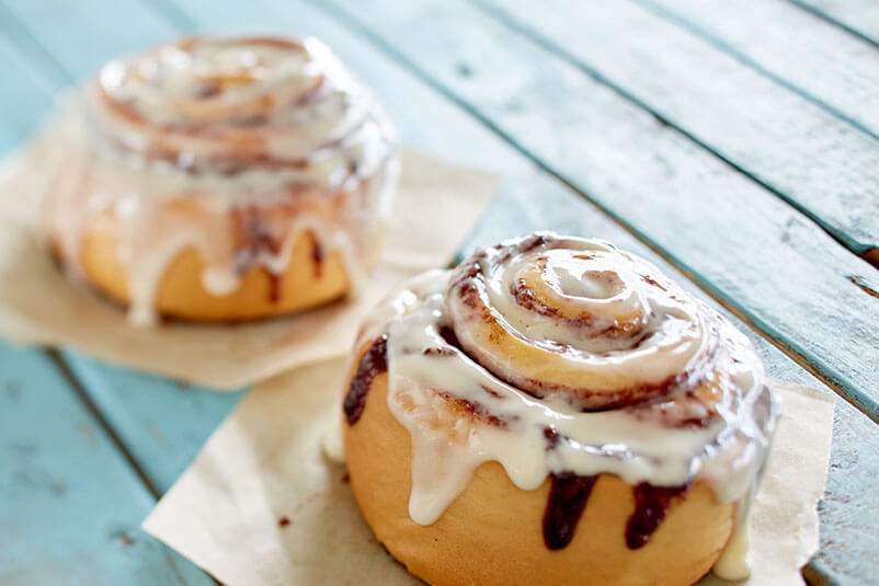 Two cinnamon buns on a blue wooden deck.