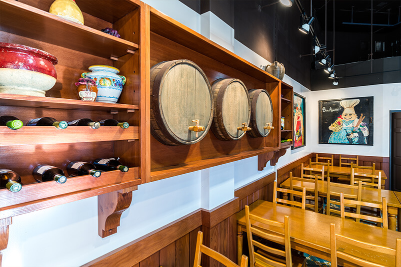Three beer wooden kegs in the wall, beside a wine rack with tables and chairs underneath.