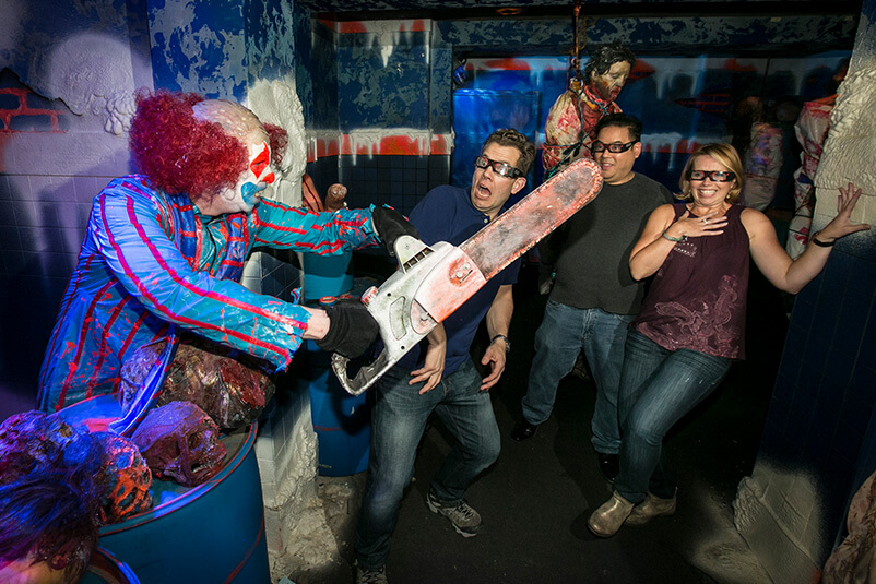 A clown holding a chainsaw scares three guests at Halloween Horror Nights.