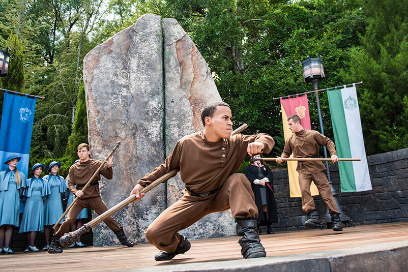Three people dressed up as the Durmstrang Harry Potter characters, one low to the ground with a pole in his hand.