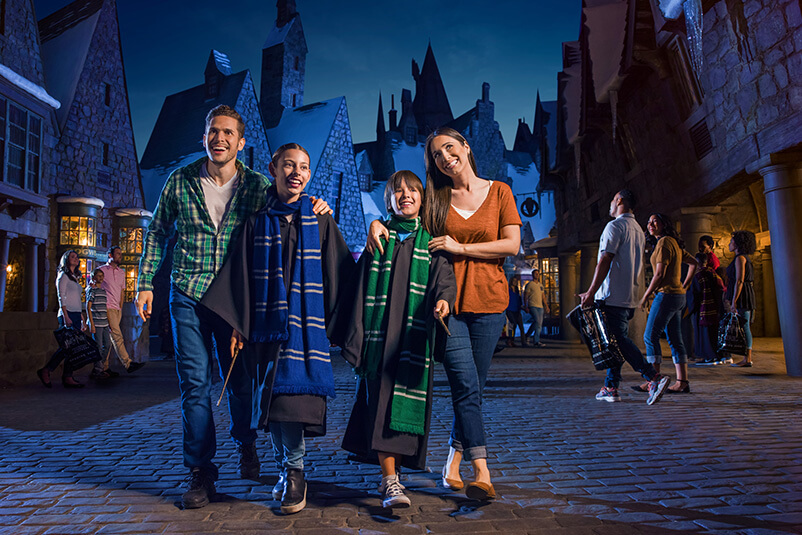 Family with two young boys dressed up as Harry Potter characters and a dark blue buildings behind them.