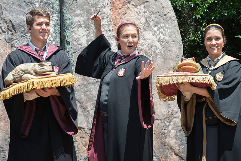 Two people holding large frog figures and one waving a wand.