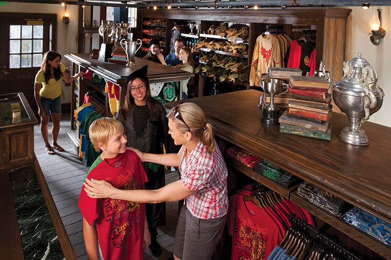 A mother holding a red t-shirt up to her son with a clerk helping in a Harry Potter themed store.