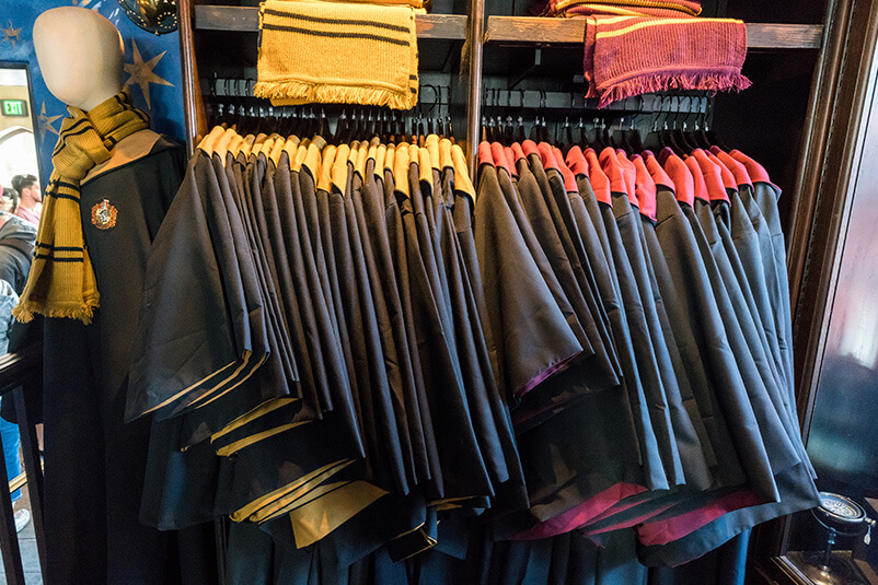 Multiple black wizard ropes hanging in a retail store with red and yellow scarfs on the shelf above.
