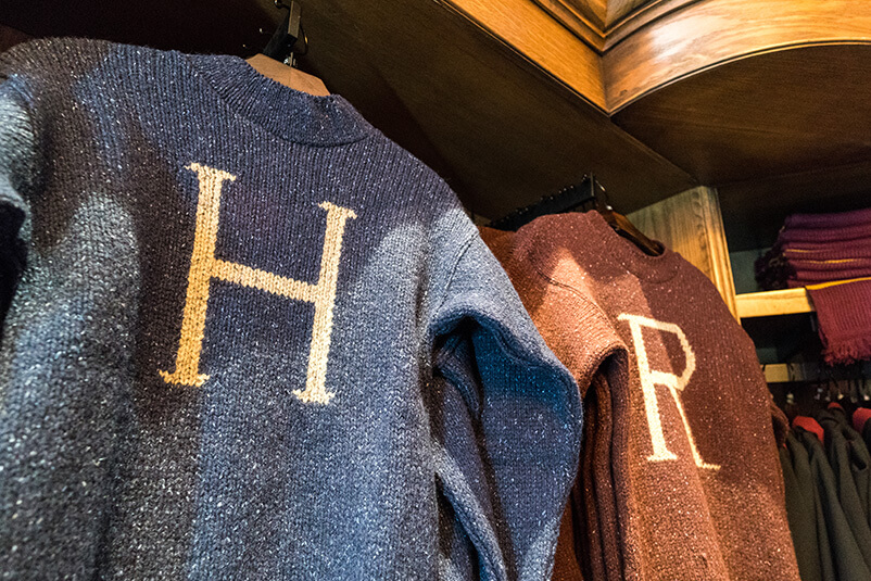 Two knitted sweaters hanging, one is blue with a H and one is red with a R.