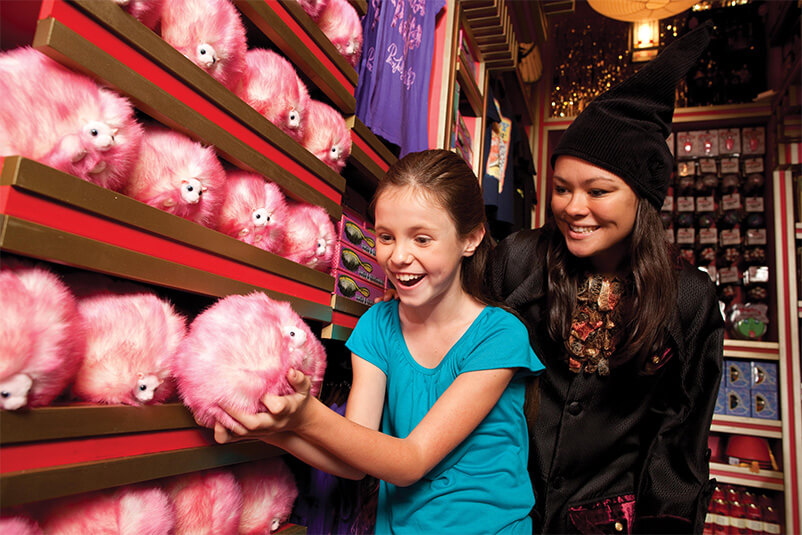 A girl holding a pink furry ball with a store clerk smiling.