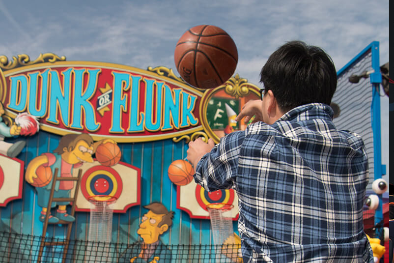 A boy throwing a basketball into the Dunk or Flunk game.