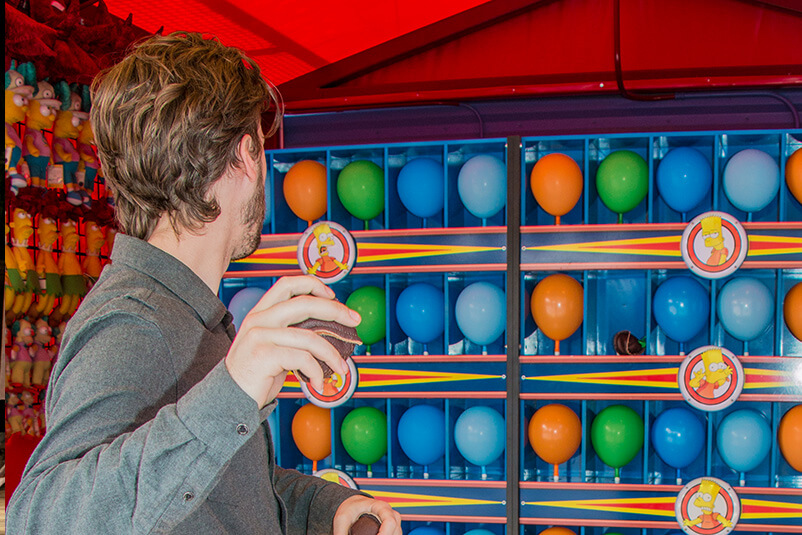 A man getting ready to throw a ball at a row of Balloons at the Carnival.