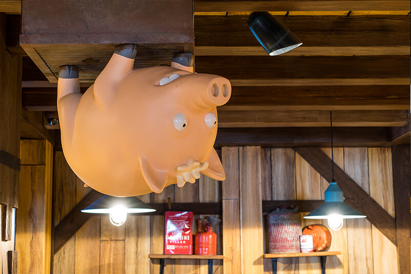 An upside down pig on a ceiling with a wooden wall behind it.