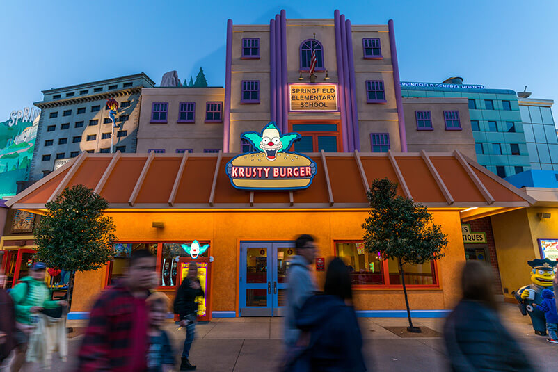 The Krusty Burger building in front of Springfield Elementary School at sunset.