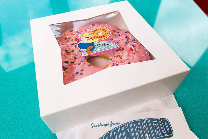 A donut with pink icing in a box from Lard Lad donuts.