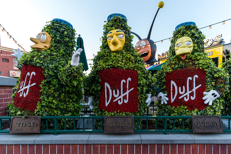 Three bushes in shapes of people and all have a yellow face and Duff on their fronts.