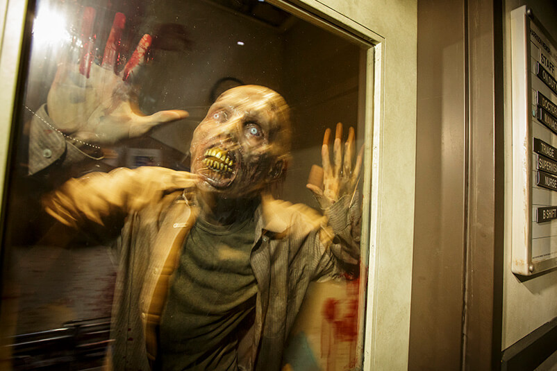 A zombie pushed up against the glass with blood on his hands.