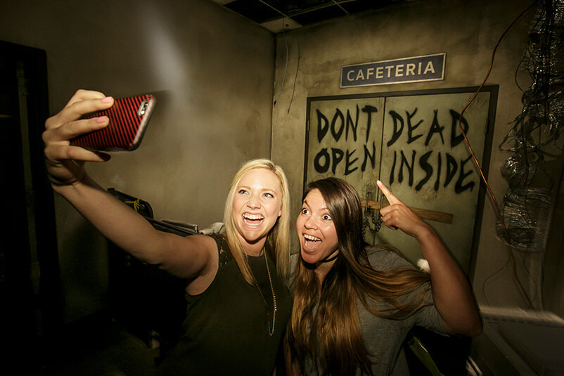 Two girls taking a selfie in front of two doors with writing saying 