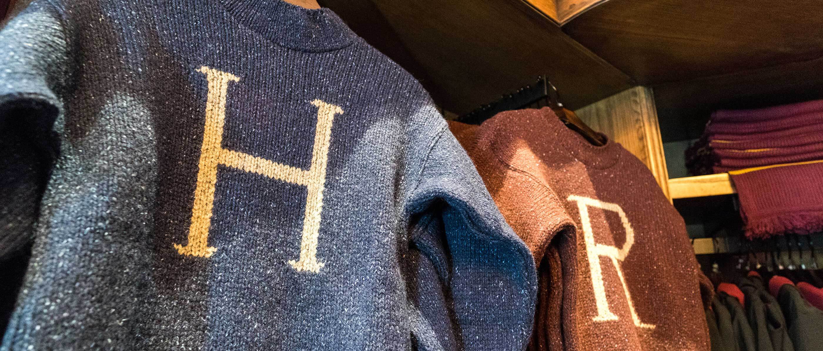 Up Close to two knitted sweaters hanging, one is blue with a H and one is red with a R.