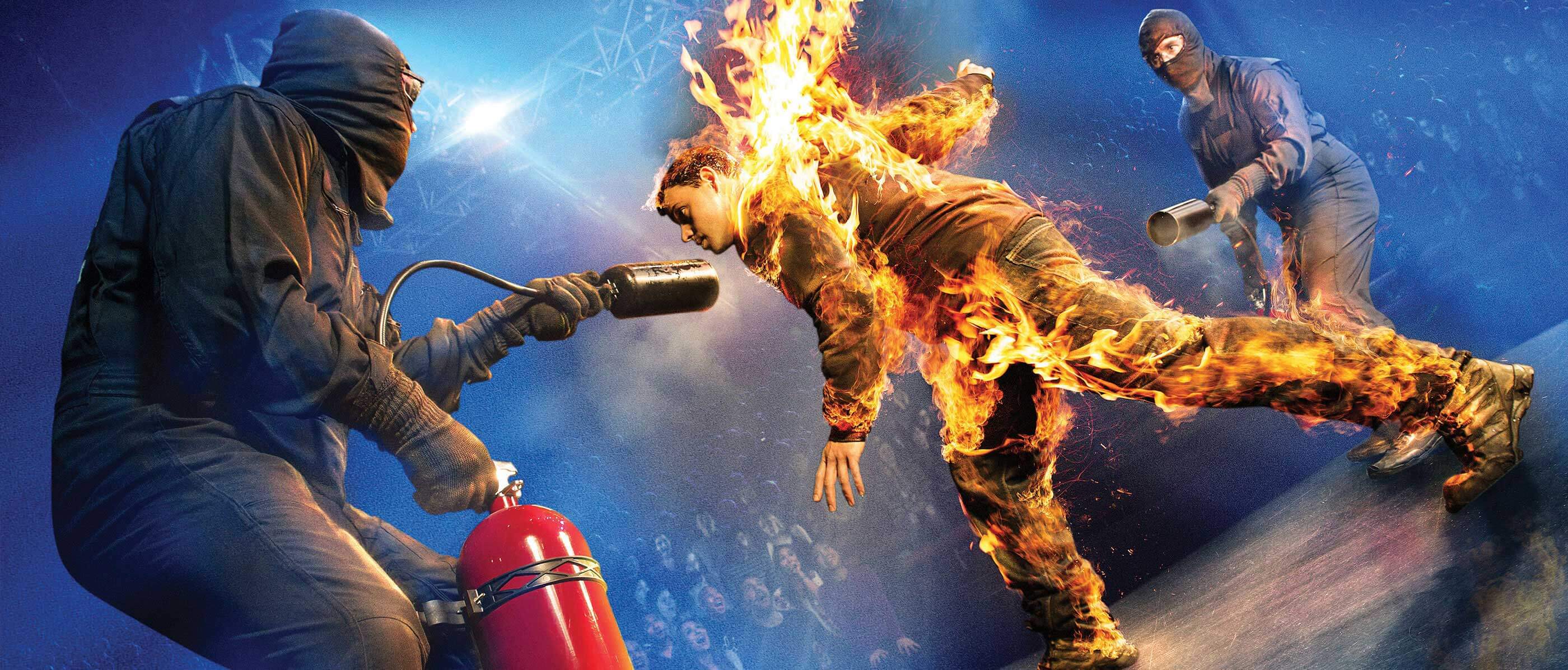 A show with a man on fire and two men with fire extinguishers putting him out.