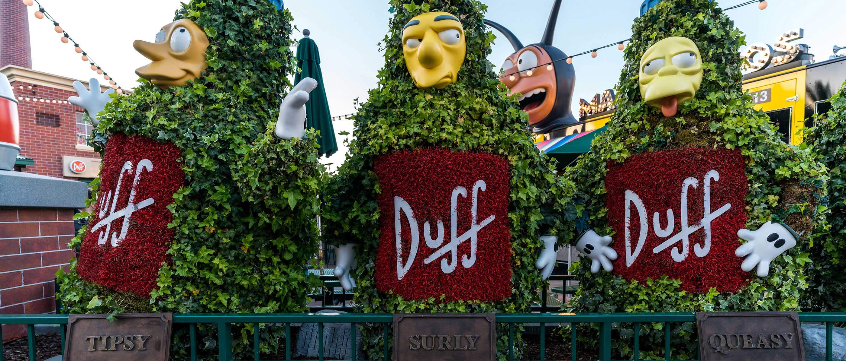 Three bushes in shapes of people and all have a yellow face and Duff on their fronts.