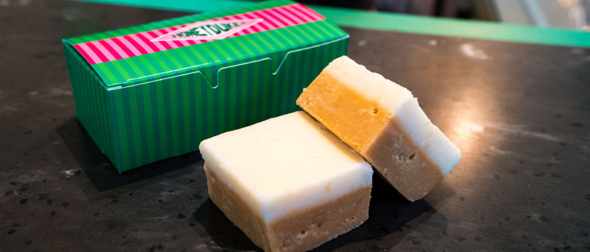 Two squares of ButterBeer Fudge with pink and green packaging